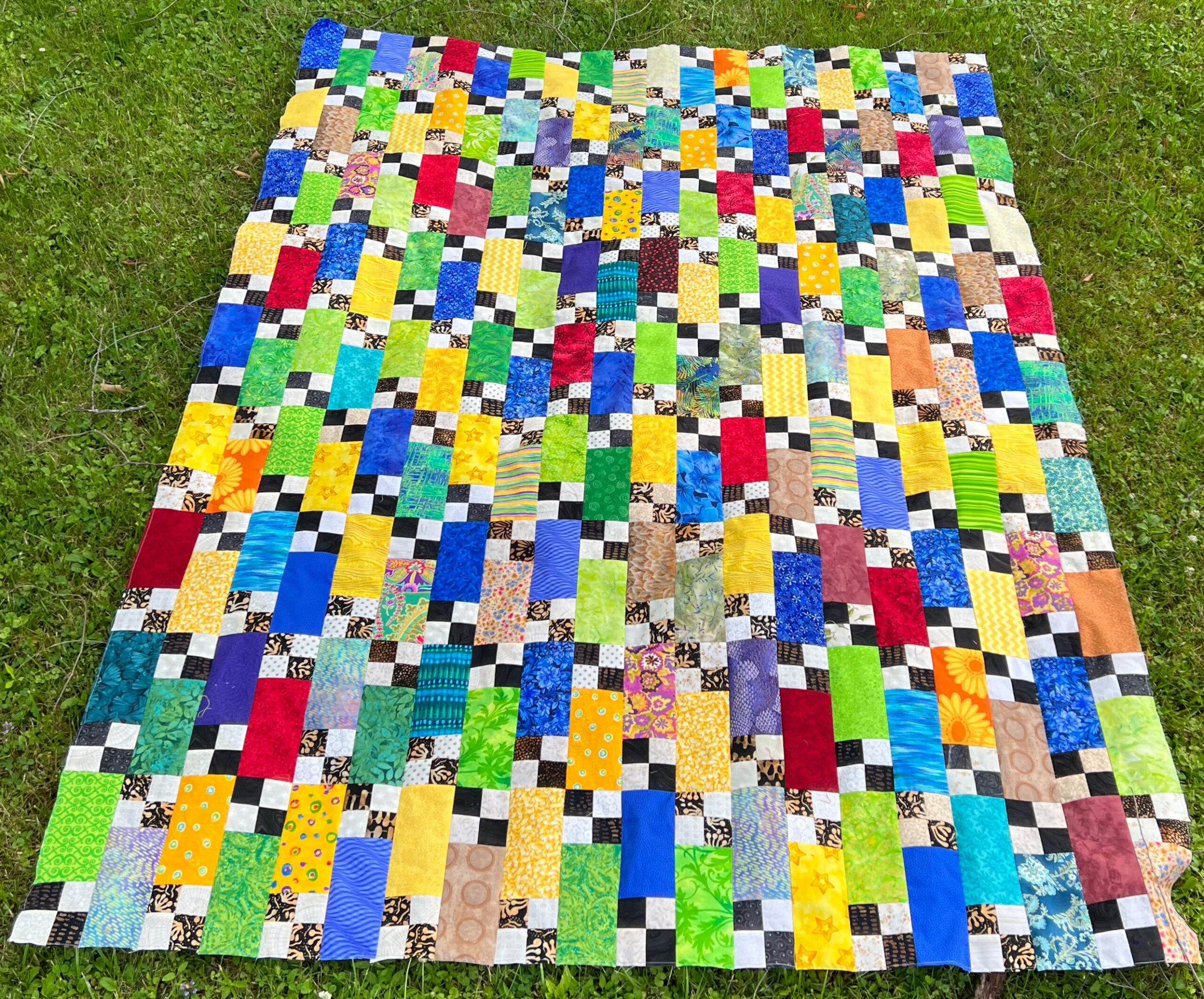 Bright quilt top with black and cream checkerboard squares, on green grass.