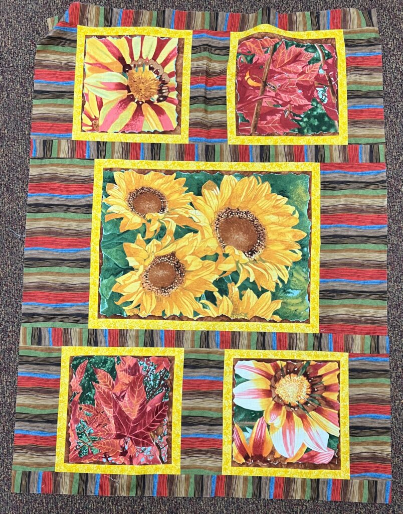Sunflower quilt with three sunflowers and two fall leaves blocks, surrounded by stripes.
